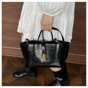 Detail of black oil wax leather bucket bag with gold lock on a white dress model