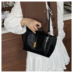 Close-up of black oily leather tote bag with vintage gold twist lock on wooden background