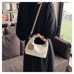 Close-up of white pleated handbag with khaki ruched handle and brand tag detail