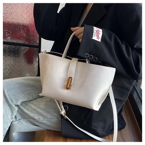 Close-up of a white leather bucket bag with a golden metal buckle held by a model