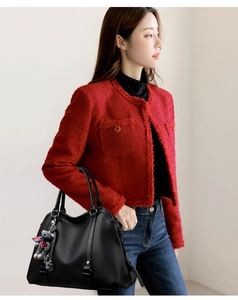 Detail of black litchi texture handbag with plush bear charm on red jacket model