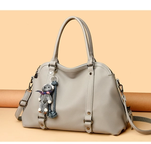 Detail of grey lychee pattern handbag featuring metal rivets and cute bear charm