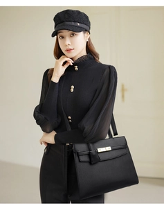 Detail of black pebbled leather handbag with gold metal clasp on model in chic outfit
