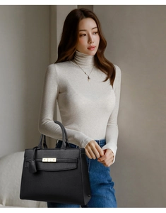 Detail of black pebbled leather tote bag with gold hardware held by a woman