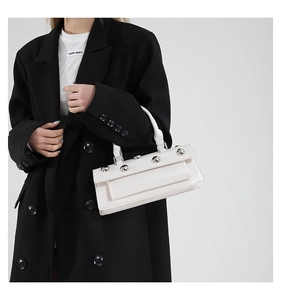 Close-up of white leather rectangular handbag with silver studs and structured handle