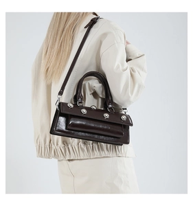 Detail of dark brown glossy leather handbag with silver rivets and dual handle straps