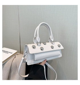 Close-up of white leather handbag with silver metallic studs and detachable strap