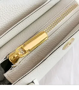 Detailed close-up of white lychee leather texture and shiny gold metal zipper on handbag