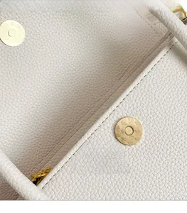 Detailed macro view of gold-tone magnetic clasp on white lychee grain leather handbag