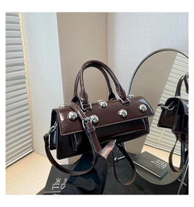 Detail of dark brown glossy leather handbag with large silver rivets and dual handles
