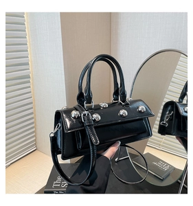 Close-up of black glossy patent leather bag with silver studs and long shoulder strap