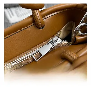 Detailed close-up of the silver metal zipper and fine stitching on a brown leather bag