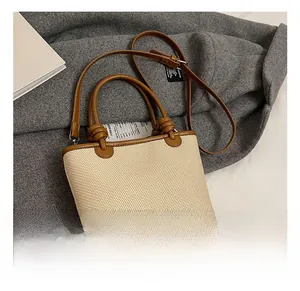 Detail of woven cream bucket bag featuring brown leather trim and knotted handle accents