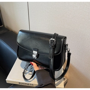 Detail of black glossy square bag with silver metal buckle and slim shoulder strap