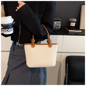Detail of woven bucket bag featuring brown leather handles with unique knotted accents