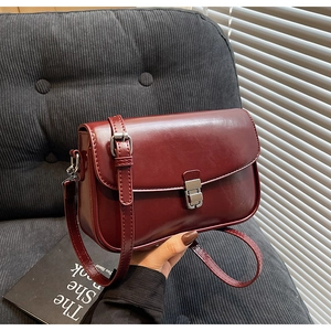 Detail of burgundy crossbody square bag with silver metal buckle on corduroy background
