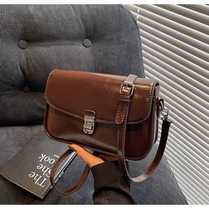 Close-up of a dark brown glossy PU leather crossbody bag with silver buckle detail