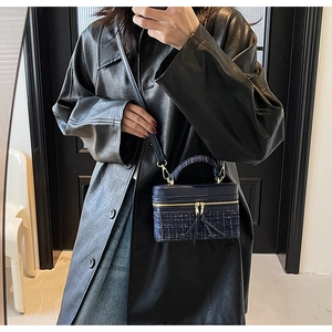 Détail du sac boîte en tweed bleu marine avec zips dorés porté sur manteau noir