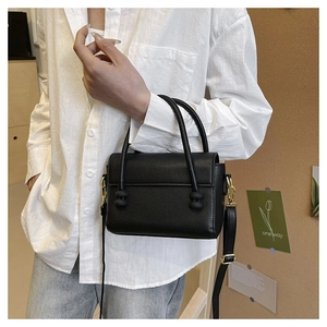 Close-up of black lychee grain leather handbag with gold hardware and spherical detail