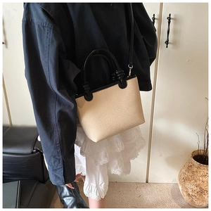 Detail of woven straw bucket bag with black leather handles and crossbody strap