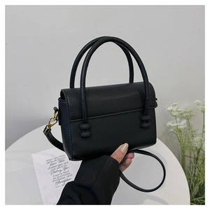 Detail of black lychee grain leather handbag with gold accents and dual ball handle decor