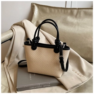 Detail of woven straw tote bag with black leather handles and knot decorative accents