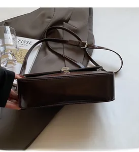 Detail of deep brown glossy square shoulder bag with silver metallic buckle on suit