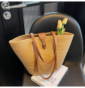 Dettaglio di una borsa tote in paglia intrecciata con manici in pelle marrone su sedia