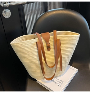 Dettaglio di una grande borsa tote in paglia con manici in pelle marrone su sedia