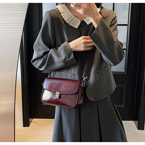 Detail view of burgundy leather crossbody bag with silver buckle worn by a model