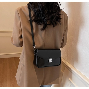 Crossbody view of a black minimalist square bag with silver metal buckle on a model