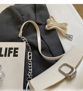 Detail of off-white faux leather saddle bag with square metal buckle on a grey blazer