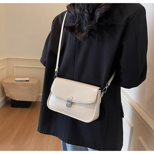 Detail of cream rectangular crossbody bag featuring silver metallic buckle on black blazer