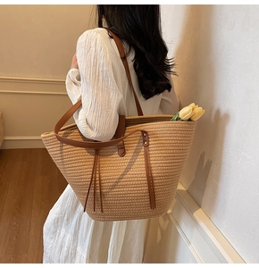 Dettaglio della grande borsa tote in paglia con manici in pelle marrone e frange