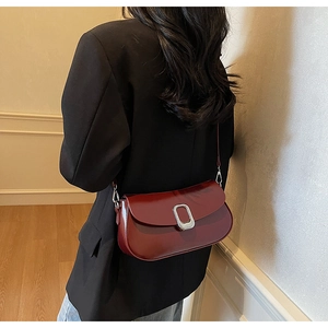 Close-up of a burgundy leather shoulder bag with a round silver buckle on a black blazer