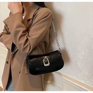 Detail of black glossy leather underarm bag with silver buckle and chain strap on a model