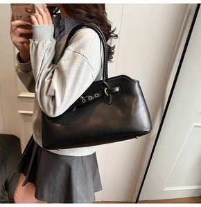 Detail of black leather tote bag featuring gold metal eyelets and a minimalist shoulder strap