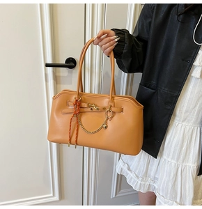 Detailed shot of leather handbag with gold chain and woven pendant on white background