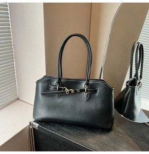 Detail of minimalist black faux leather tote bag with elegant gold hardware on wood surface