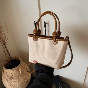 Minimalist beige woven bucket bag with brown leather straps and vintage knot design