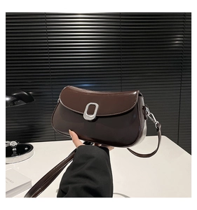 Detail of dark brown leather underarm bag featuring a metallic oval buckle and smooth finish