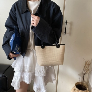 Straw tote bucket bag in beige with black knotted handles worn by a model in casual style