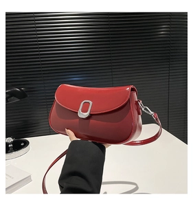 Close-up of a glossy red patent leather shoulder bag with a rectangular silver metal buckle