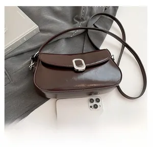 Detail of glossy brown underarm bag with silver buckle next to a smartphone