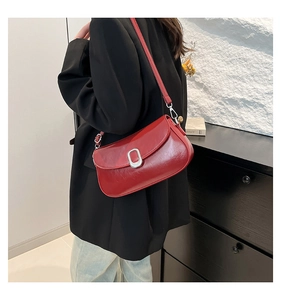 Close-up of red patent leather underarm bag with silver oval buckle worn by model