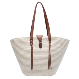Large cream straw tote bag with brown leather handles and tassel detail on white background