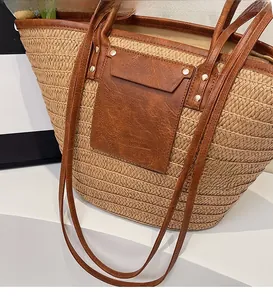 Detail of woven straw tote bag with brown leather handles and golden rivet accents