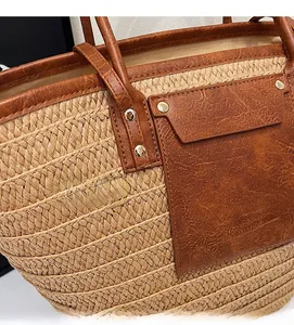 Detail of hand-woven straw tote bag with brown faux leather trim and golden metal rivets