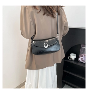 Detail of a black glossy shoulder bag with silver metal buckle on a model from the back