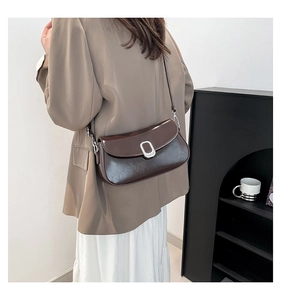 Detail of a brown glossy leather shoulder bag with vintage texture and silver buckle